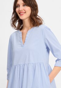 Blau-weiß gestreifte Bluse mit lässiger Passform, Stehkragen, Dreiviertelärmeln und gerafftem Bund, ausgestattet mit Seitentaschen.