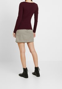 Burgundská pruhovaná dlouhá halenka spárovaná s texturovanou mini sukní v houndstooth vzoru. Černé kotníkové boty se zipy a úchyty dokončují vzhled.