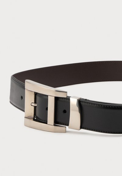 Ceinture en cuir noir avec une boucle rectangulaire en métal argenté et une boucle assortie, montrée partiellement enroulée sur un fond blanc.