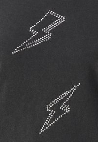 Zwart stof met twee bliksemflitsontwerpen gemaakt van kleine zilveren rhinestones, diagonaal op het oppervlak geplaatst.