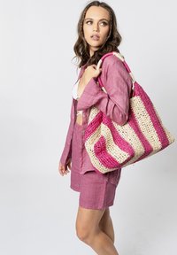 Grote geweven draagtas met roze en beige strepen, gemaakt van een stro-achtige stof, met stevige handvatten.