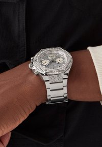 Montre analogique en argent avec un boîtier octogonal, des accents en diamant et un bracelet en métal, affichant un cadran texturé argenté avec trois sous-cadrans.