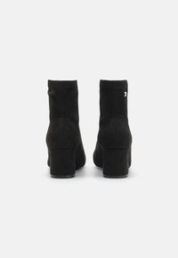 Stivaletti neri in suede fino alla caviglia con punta arrotondata e tacco a blocco. Presentano cuciture minime e un piccolo logo accentato sul tacco.