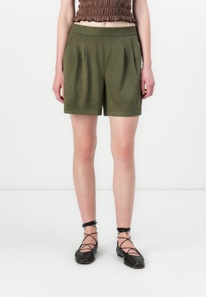 Shorts vert olive avec des plis, fabriqués en matériau doux. Associés à un haut marron ajusté et des ballerines noires avec des lanières à la cheville.