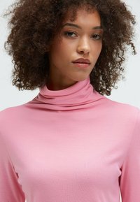 Pink turtleneck top with a smooth, soft texture and slim fit, featuring a high neckline and long sleeves.
