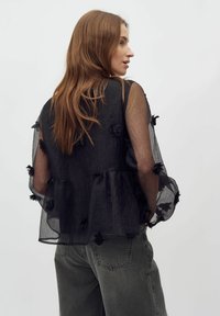 Must musta blouse, millel on tekstureeritud kangas, kihiline peplum äär ja lillede kaunistused. Kanda oli oliiviroheliste kõrge vöökohtadega pükste peal.