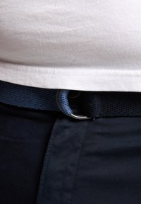 Marineblauwe geweven riem met een zilveren metalen D-ring. Gecombineerd met een wit T-shirt en een donkere broek, wat een casual look laat zien.