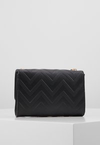 Czarna kopertówka z pikowaniem w kształcie jodełki, eleganckim prostokątnym kształtem i złotymi elementami ozdobnymi. Wykonana z teksturowanego syntetycznego materiału.