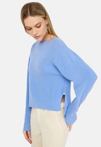 Maglione corto azzurro chiaro con texture a coste, maniche larghe, scollo rotondo e spacchi laterali con dettagli a bottoni. Ideale per essere indossato a strati.