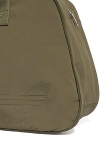 Olivengrønn duffelbag med teksturert overflate, som har en fremtredende preget logo og en sølvfarget glidelås. Kompakt og slitesterk design.