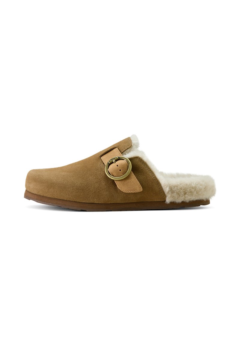 Brown suede slipper featuring a soft, fluffy white lining, a round metal buckle accent, and a slightly curved shape. Flat sole design.