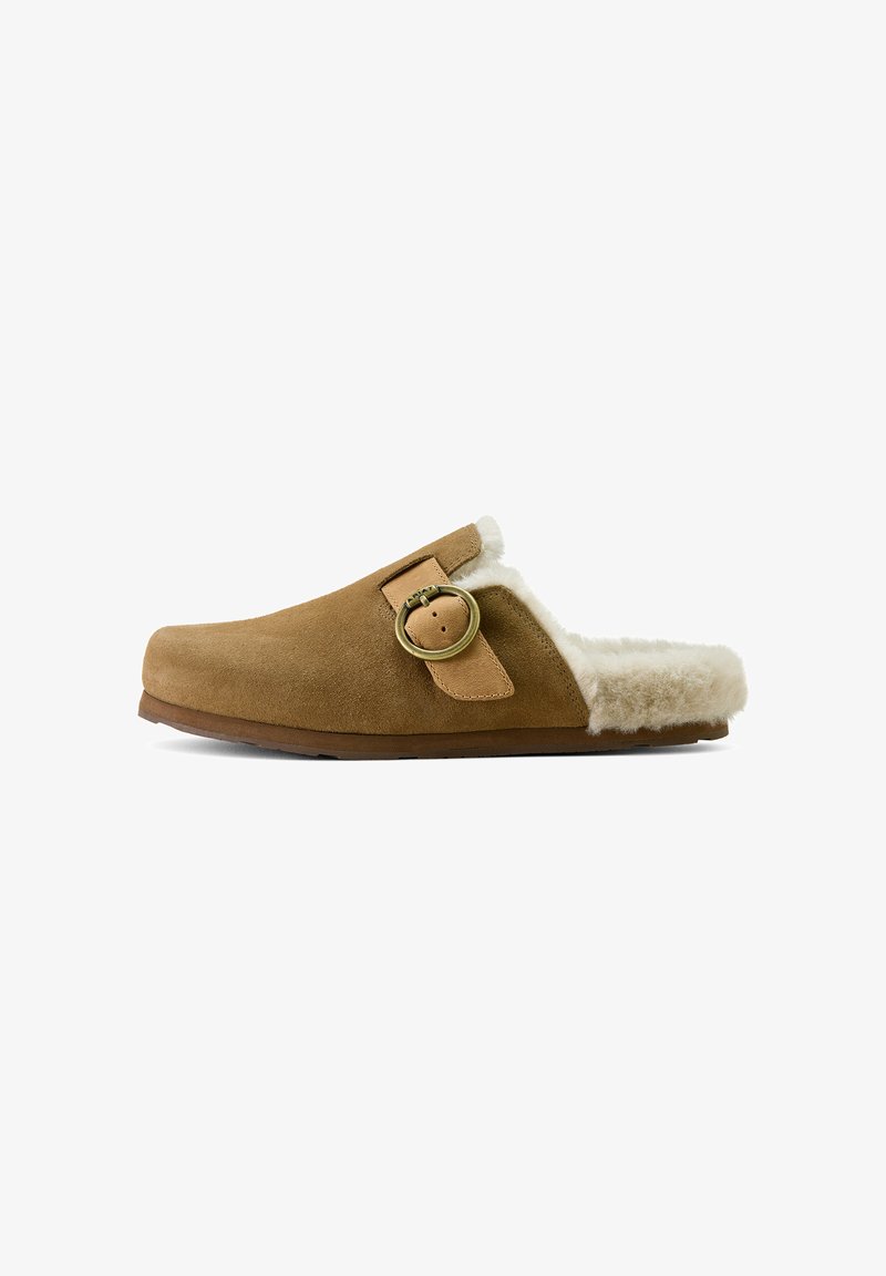Brown suede slipper featuring a soft, fluffy white lining, a round metal buckle accent, and a slightly curved shape. Flat sole design.