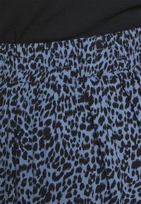 Blauer Stoff mit einem schwarzen Leopardenmuster, einem elastischen Bund und dezenten Faltendetails für zusätzliche Textur.