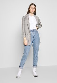 Grå rutete blazer med lyseblå høyhårede jeans, hvit polo-skjorte og hvite høye sneakers med svarte detaljer.
