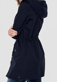 Navy blue waterproof jacket with a hood, drawstring waist, and buttoned pockets. Features a sleek design and smooth texture.