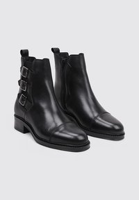 Botines de cuero negro hasta el tobillo con punta cuadrada, tres hebillas en el lateral y una cremallera en el costado. Tacón plano y textura suave.