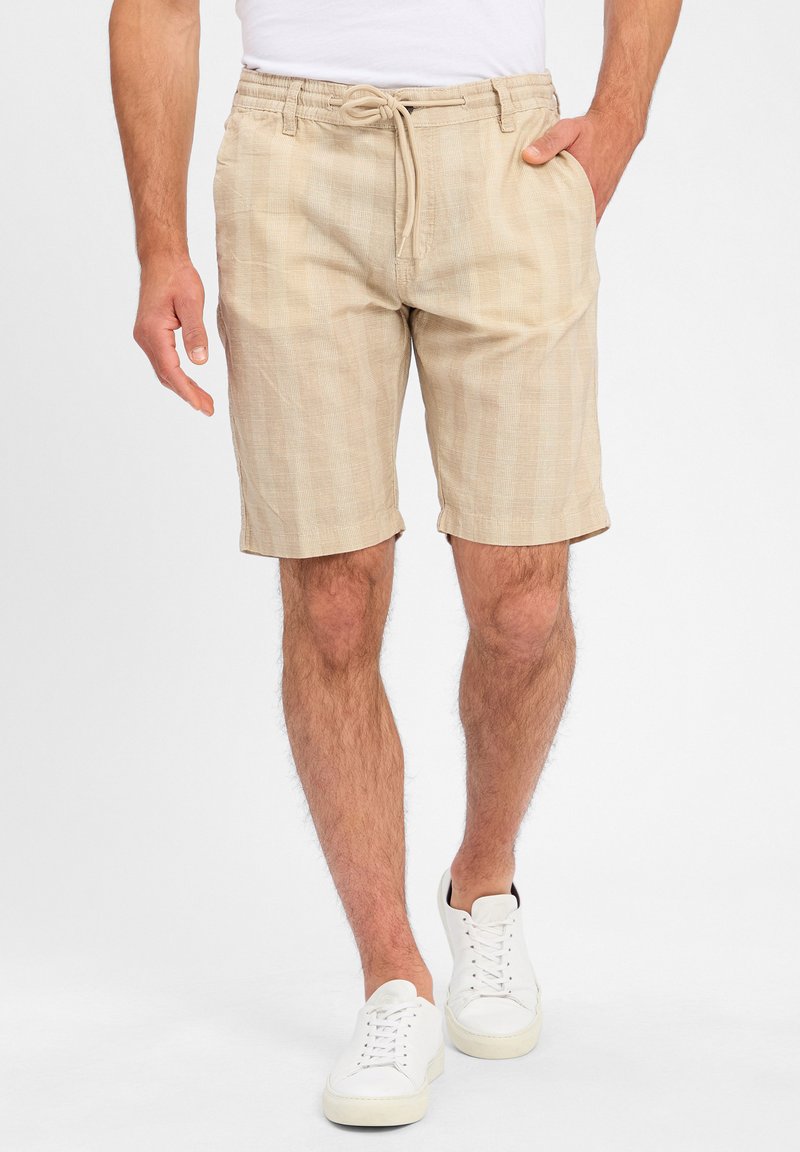 Beige linen shorts with an elastic waistband and drawstring. Casual fit, knee-length, featuring a subtle textured pattern.