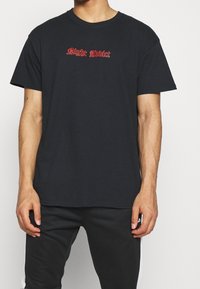 Svart bomullströja med korta ärmar, med röd broderad text "Night Addict" centrerad på bröstet, avslappnad passform och rundad hals.