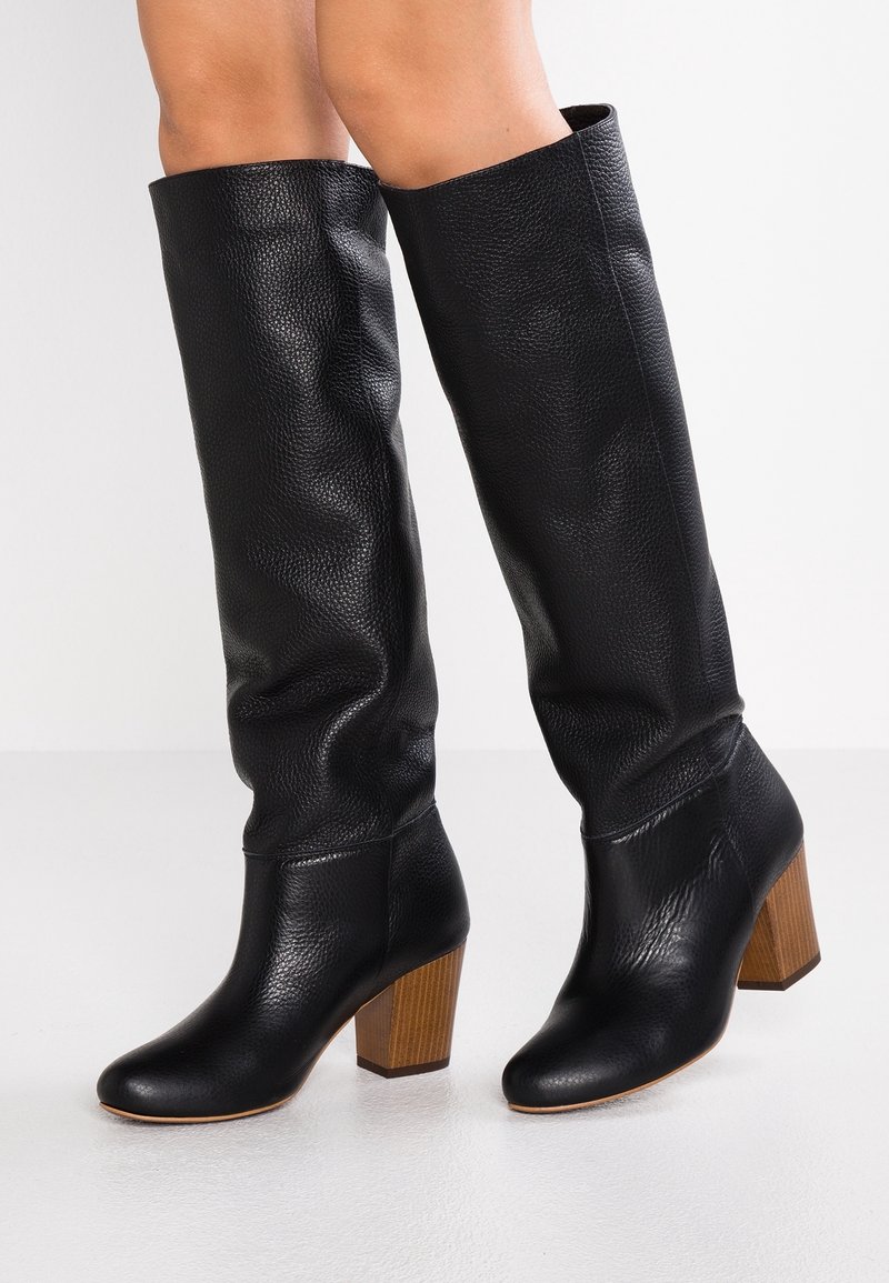 Bottes en cuir noir, montantes jusqu'au genou, avec une surface texturée, un bout arrondi et un talon en bois robuste. Fini lisse avec des plis discrets.