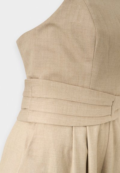 Κοντινό πλάνο μπεζ φόρεμα από λινό με φαρδιά, διπλωμένη ζώνη μέσης και δομημένες ραφές στο μπούστο και πτυχές στην φούστα.