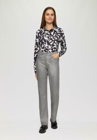 Blouse à manches longues avec un motif abstrait bleu marine et blanc, associée à un pantalon gris taille haute et des chaussures à plateforme noires.