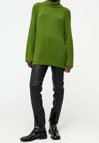 Groene geribbelde coltrui met lange mouwen, gecombineerd met zwarte leren broek met zijsplits en glanzende zwarte enkellaarsjes.