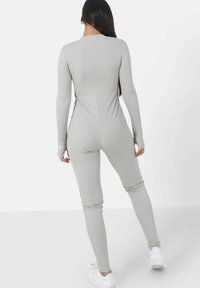 Bodysuit de manga larga en gris claro con un diseño ajustado, textura acanalada y agujeros para los pulgares en los puños, combinado con zapatillas blancas.