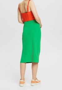 Haut court rouge à bretelles fines associé à une jupe midi verte. Baskets avec des accents orange et une semelle épaisse. Texture lisse partout.