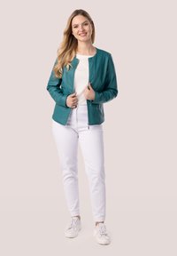 Giacca di pelle verde acqua con colletto rotondo, zip frontale e due tasche, abbinata a pantaloni bianchi e sneaker bianche. Texture liscia.