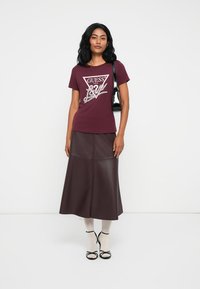 Bordeaux kortemouw t-shirt met een wit grafisch logo, gecombineerd met een lange bruine faux leren rok en zwarte sandalen met enkelbandje.