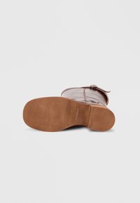 Καφέ δερμάτινη μπότα με λεία επιφάνεια, στρογγυλεμένη μύτη και επίπεδη ταμπά λαστιχένια σόλα. Διαθέτει διακοσμητικό λουράκι και λεπτομέρεια με αγκράφα.