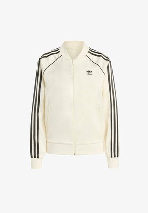 Ljusgrå bomberjacka med svarta ränder på ärmarna, ribbade muddar och krage. Har dragkedja och sidofickor. Adidas-logotyp på bröstet.