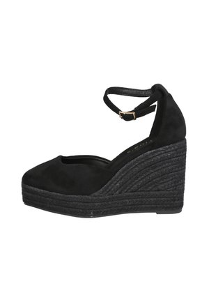 Zapato de cuña negro con puntera cerrada, correa en el tobillo y suela de plataforma trenzada, mostrado de perfil sobre fondo blanco.