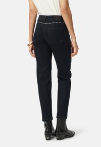 Pantalones vaqueros de mezclilla azul oscuro con un corte ajustado, que presentan una cinturilla con tachuelas y bolsillos traseros, combinados con botas negras de tobillo.
