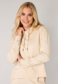 Beige hoodie met een ontspannen pasvorm, voorzien van een trekkoord en geribbelde manchetten. Glad materiaal met een gelaagde zoomdetail.
