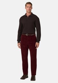 Herroutfit bestående av en strukturerad mörkbrun långärmad skjorta, vinröda kordbyxor och bruna läderskor, stylat med ett mönstrat bälte.