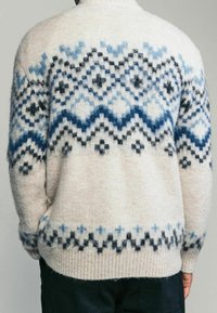 Pull en laine avec une base crème et des motifs géométriques bleus et noirs. Texture en tricot épais et finitions côtelées aux poignets et à l'ourlet.