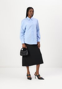 Light blue long-sleeve button-up shirt with vertical stripes, paired with a black midi skirt and black heeled shoes. Small black handbag included.