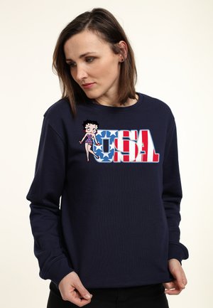 Mørkeblå sweatshirt med et farverigt "USA" grafisk design, prydet med en tegneseriefigur i et prikket outfit. Materialet virker blødt og strækbart.