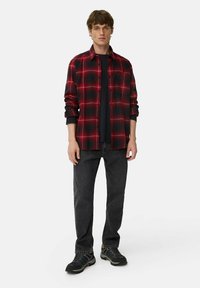Rød og sort ternet flannelskjorte med knappedyrkning, båret over en sort T-shirt, parret med mørke jeans og sorte sko.