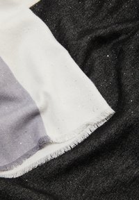 Multikleurige sjaal met witte, grijze en zwarte secties, voorzien van een zachte textuur; inclusief subtiele glinsterdetails en rafelige randen.