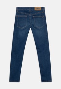 Jeans de denim azul oscuro con corte ajustado. Presentan dos bolsillos traseros, costuras visibles y un parche de cuero marrón claro con la marca en la cinturilla.