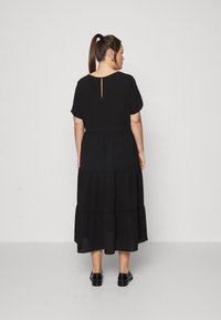 Crna midi haljina s višeslojnim krojem i kratkim rukavima, koja se ističe detaljem otvorenog leđa i opuštenim siluetom. Mekan, lepršavi materijal.