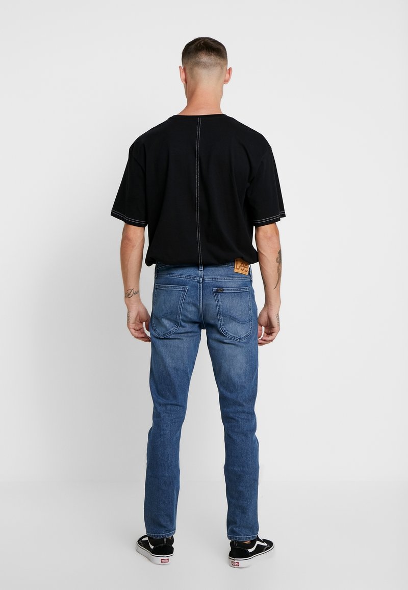 Černé oversized tričko s kontrastním prošíváním, v kombinaci s modrými denimovými džínami s jemným brandingem a rovně střiženým střihem.