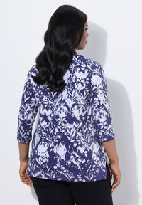Granatowa i biała bluzka w kwiatowy wzór z długimi rękawami, o luźnym kroju, z bocznymi rozcięciami i miękkiego materiału, widok z tyłu.
