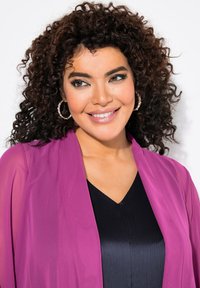 Lila, transparente Kimono mit offenem Vorderteil über einem schwarzen, strukturierten V-Ausschnitt-Oberteil; das Model hat lockige Haare und trägt silberne Creolen.