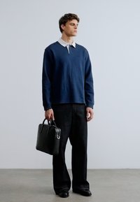 Μπλε σκούρο πόλο μπλούζα μακρυμάνικη με λευκό γιακά, σε συνδυασμό με φαρδιά μαύρα τζιν παντελόνια και μαύρη δερμάτινη τσάντα. Λεπτή υφή, μινιμαλιστικός σχεδιασμός.