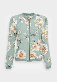 Chaqueta bomber floral en tejido verde claro. Presenta flores blancas y naranjas, cierre con cremallera, puños de canalé y un cuello redondo.