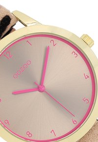 Gold-tone watch with a pink second hand, light pink textured dial, and bold pink hour markers on a soft brown strap.