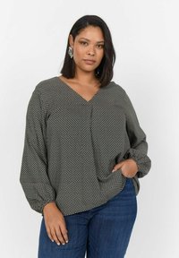 Langärmlige Bluse im schwarz-weißen geometrischen Muster, V-Ausschnitt-Design, weicher Stoff mit leichtem Glanz, kombiniert mit blauen Jeans.